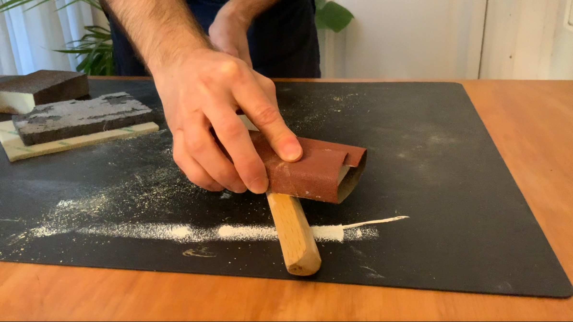 Fotografia de cómo se lijan las aristas de un Bokken en su cuidado y mantenimiento, envolviendo un taco de madera con papel de lija, 